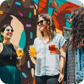 Two women enjoy drinks by a colorful mural