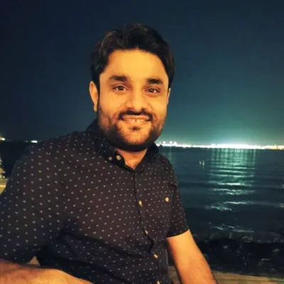 Smiling man standing near waterfront at night with city lights in background