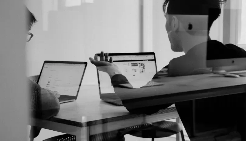 Two people in discussion at a desk with laptops, possibly reviewing a permit or visa application