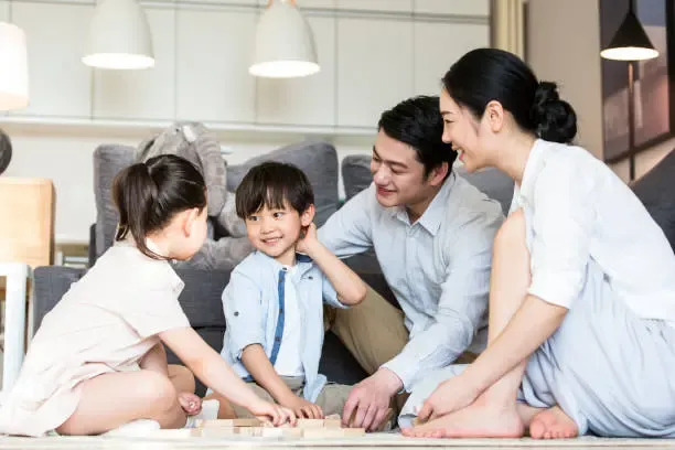 Happy family playing together at home, with parents and two children engaging in a board game on the living room floor