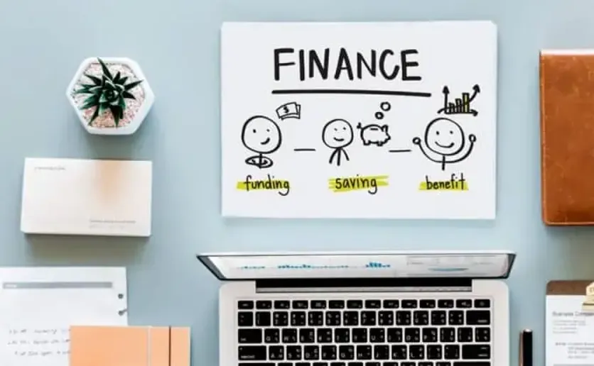 Drawing on a whiteboard showing funding, saving, and benefit icons above a workspace with a laptop and stationery