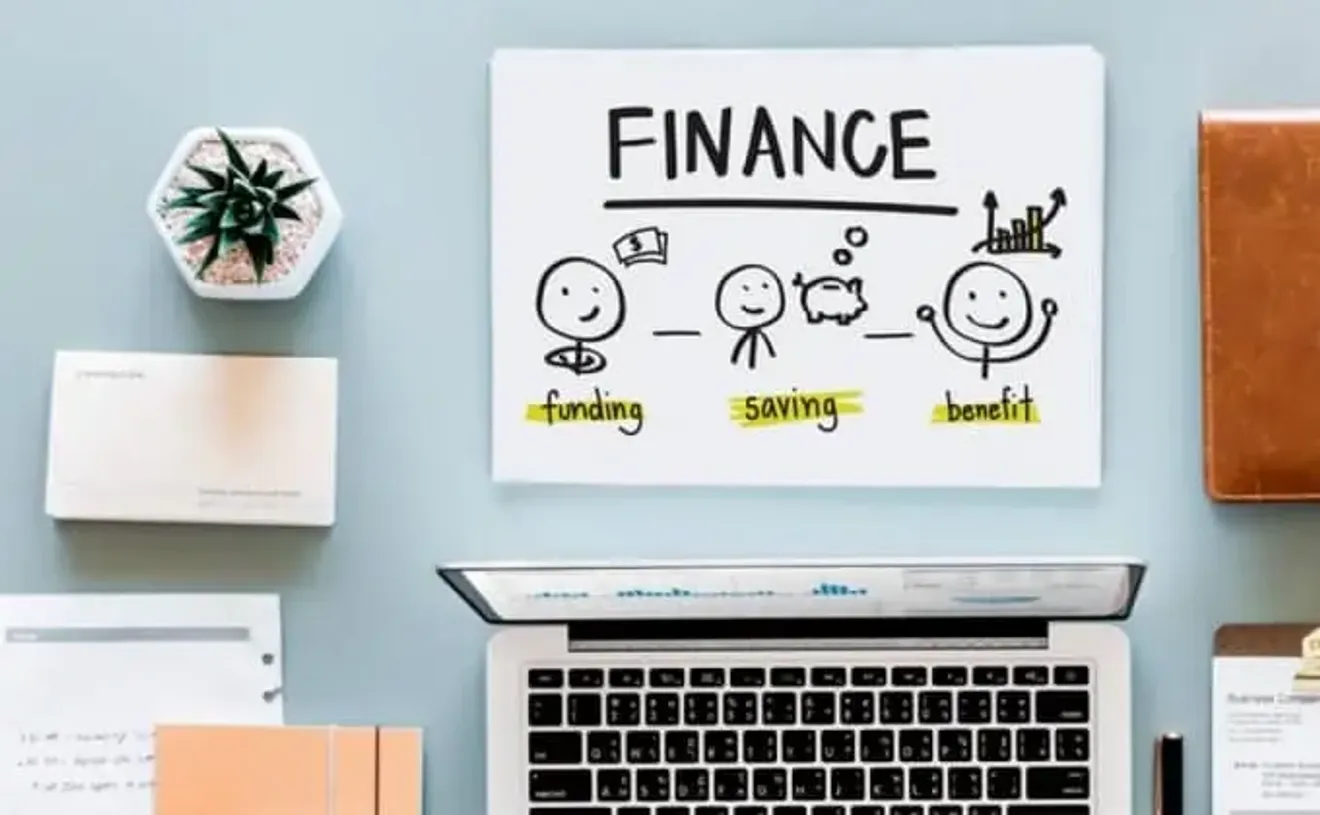 Drawing on a whiteboard showing funding, saving, and benefit icons above a workspace with a laptop and stationery