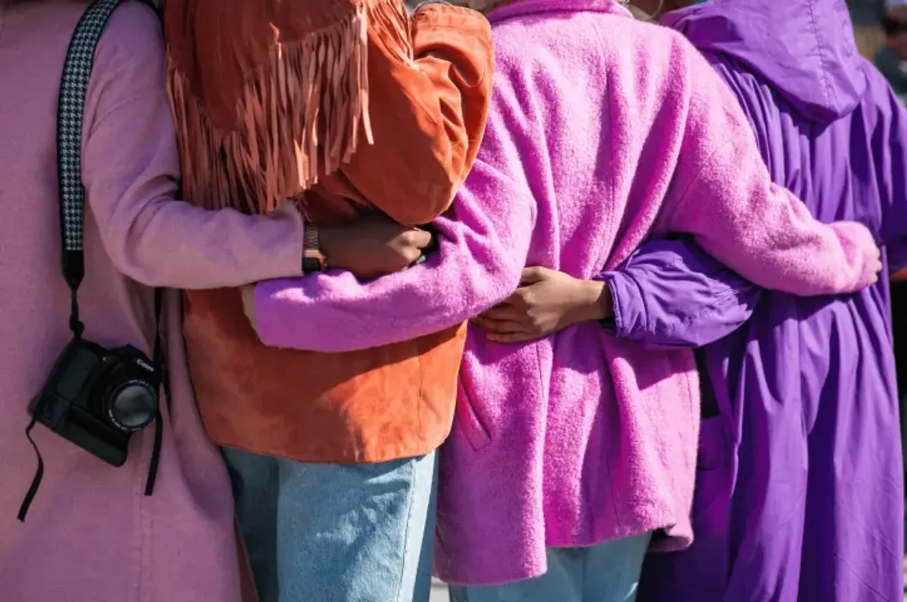 Close-up of four people wearing colorful jackets embracing in a group hug, symbolizing friendship and unity