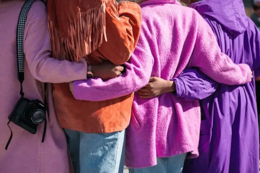 Close-up of four people wearing colorful jackets embracing in a group hug, symbolizing friendship and unity