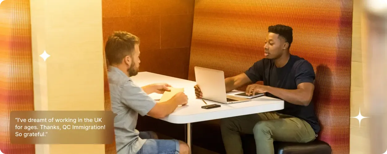 Two men seated in a booth with laptops, engaged in discussion in a modern workspace; overlaid testimonial praises UK visa support.