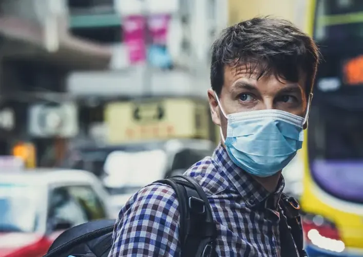Man in protective face mask walking on a busy city street during COVID-19 pandemic