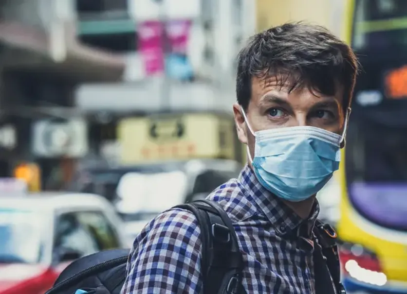 Man in protective face mask walking on a busy city street during COVID-19 pandemic