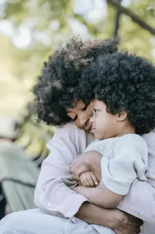 A mother lovingly hugging her child outdoors, conveying warmth and emotional connection