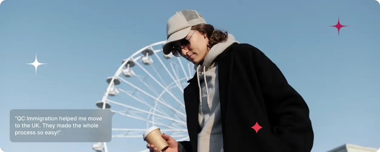 Casually dressed young person holding a coffee cup and walking near a large ferris wheel.