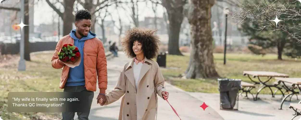 A smiling couple walks hand-in-hand through a park with the man holding a bouquet of flowers while the woman walks their dog.