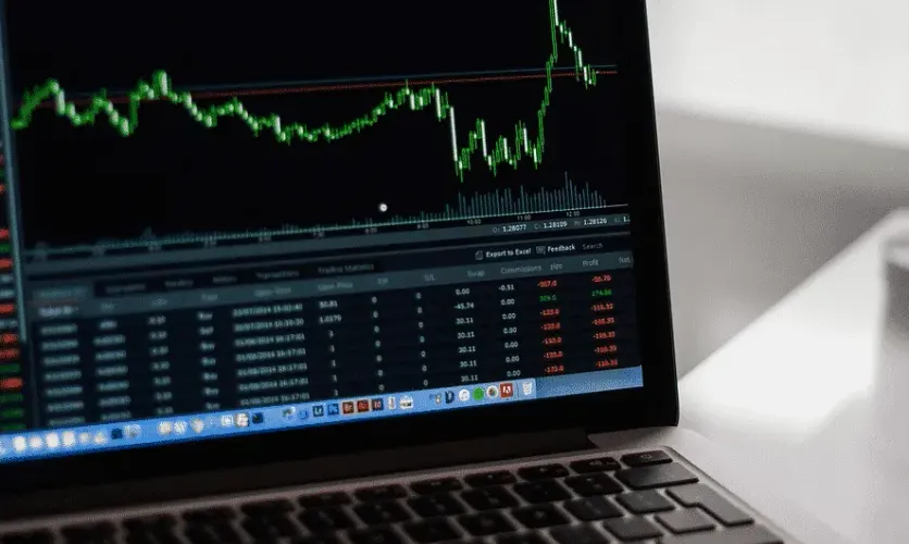 Laptop screen displaying a stock market chart with fluctuating prices and data tables.