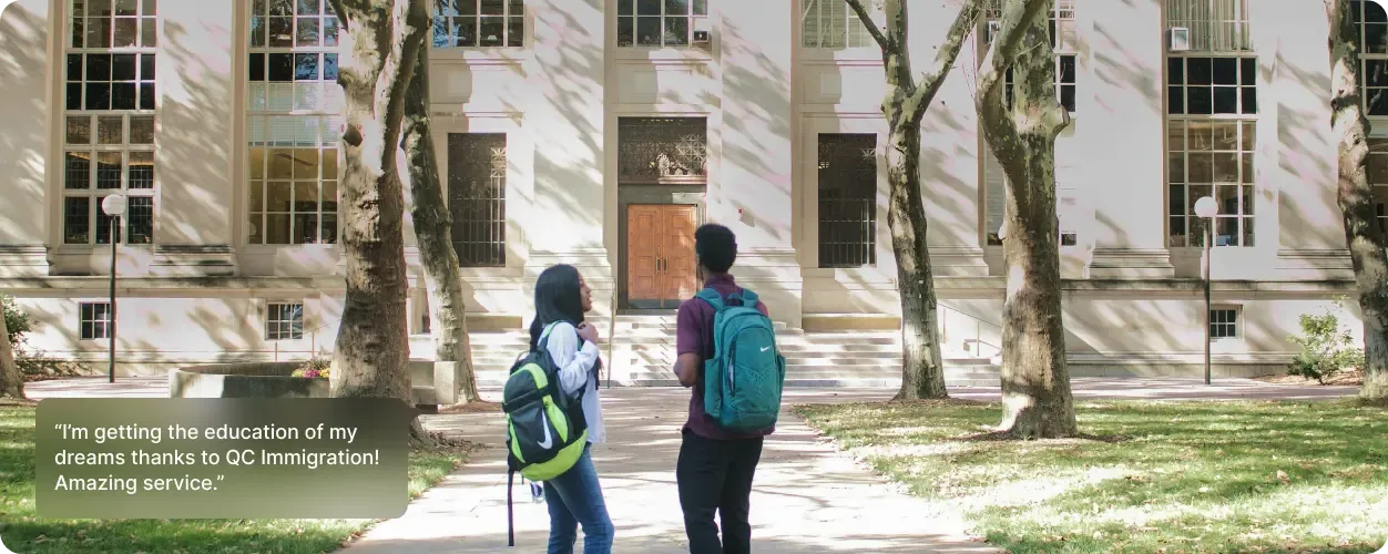Two students with backpacks walking toward a large university building on a sunny day.