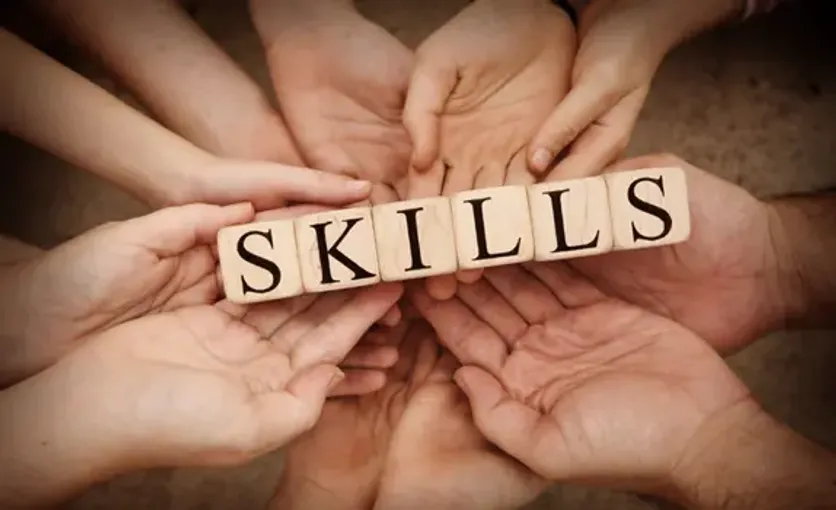 Multiple hands holding wooden blocks that spell "skills," symbolizing teamwork, collaboration, and skill development