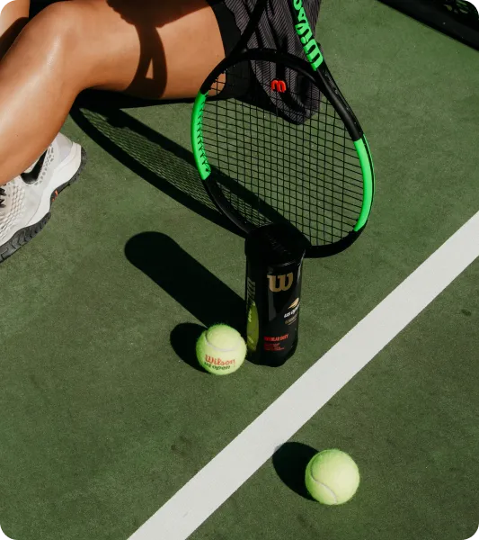 Tennis player with racket and balls on court, symbolizing athletes eligible for the UK International Sportsperson Visa