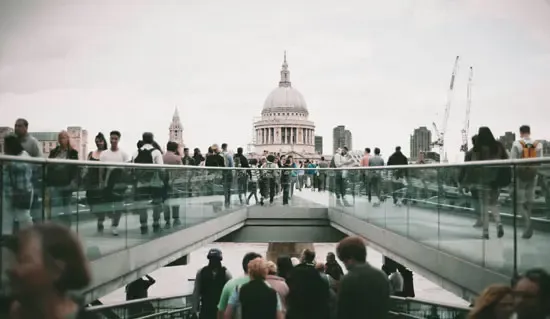 Crowd of people crossing a modern bridge with St. Paul’s Cathedral in the background, representing urban life and skilled worker migration in London