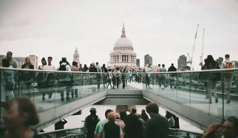 Crowd of people crossing a modern bridge with St. Paul’s Cathedral in the background, representing urban life and skilled worker migration in London