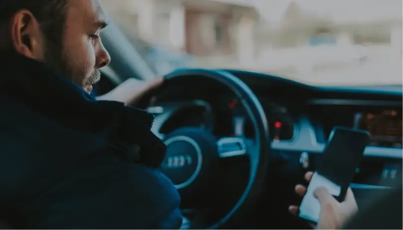 Man using mobile phone while driving, highlighting UK driving offence related to mobile use