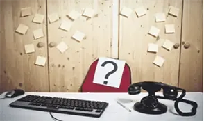 Office desk setup with headset, keyboard, and a hat marked with a question mark surrounded by sticky notes, symbolizing immigration support queries