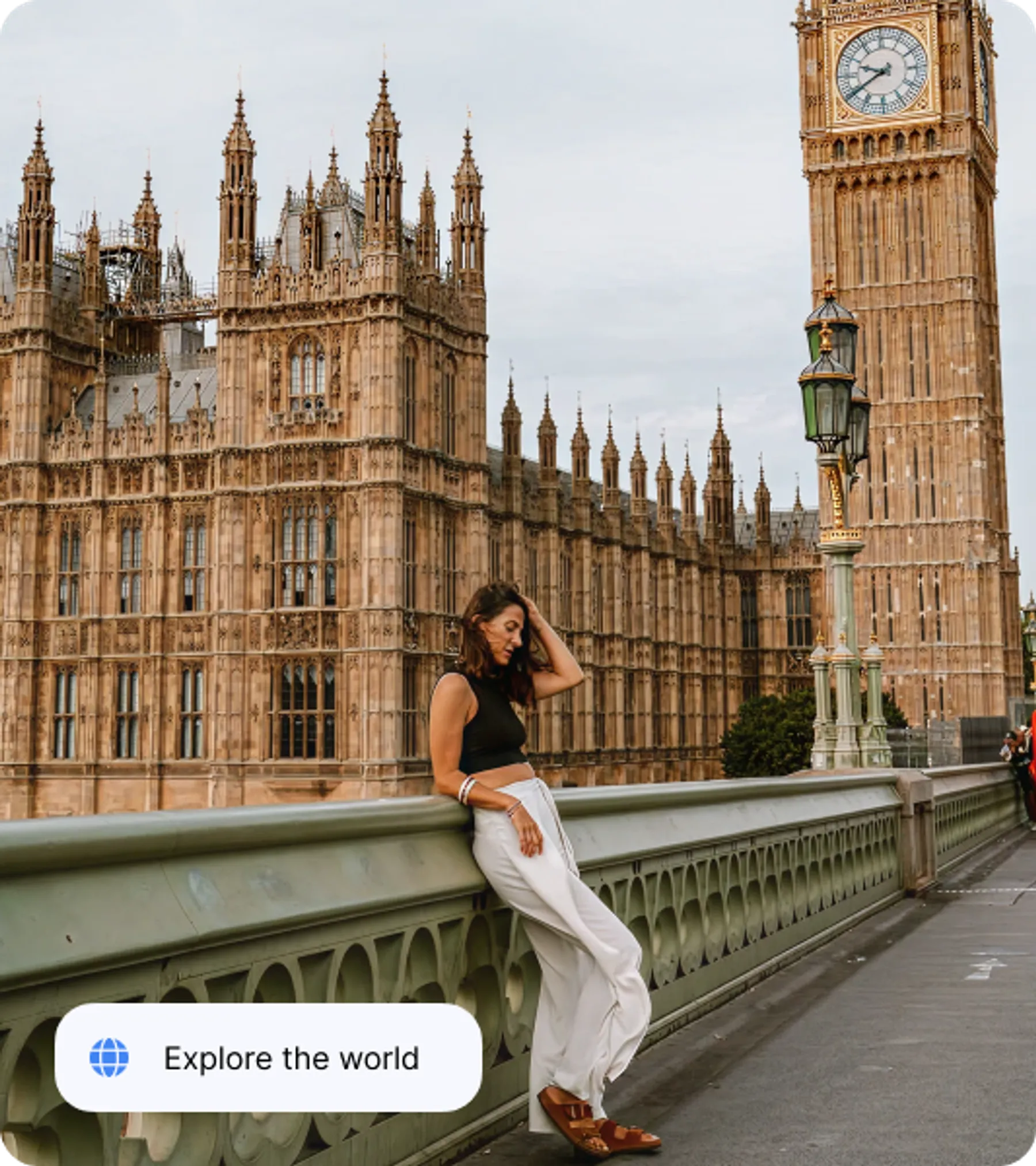 A woman in white trousers and a black top leans on Westminster Bridge with Big Ben and the Palace of Westminster behind her.