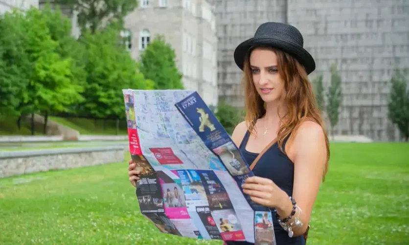 Woman wearing a hat and reading a map outdoors, representing travel and exploration.