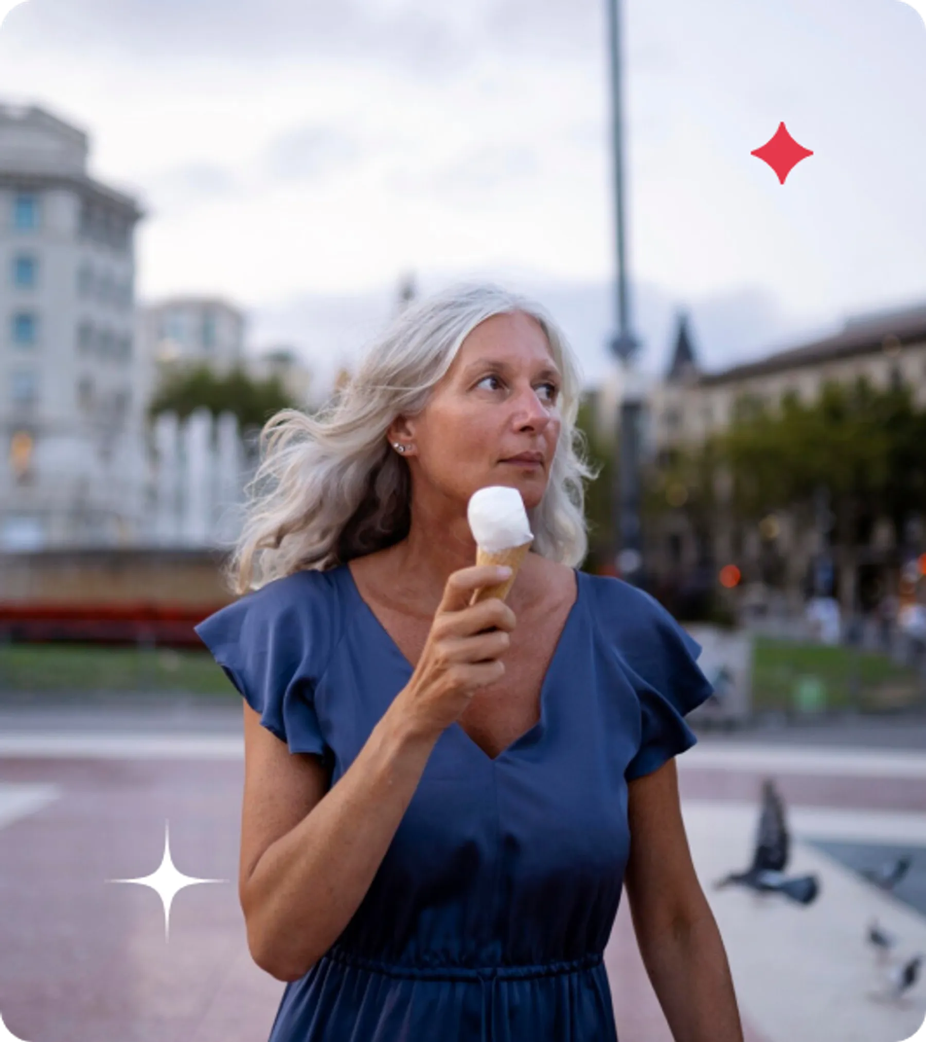 Woman with silver hair holding an ice cream cone while walking through a city square at dusk.