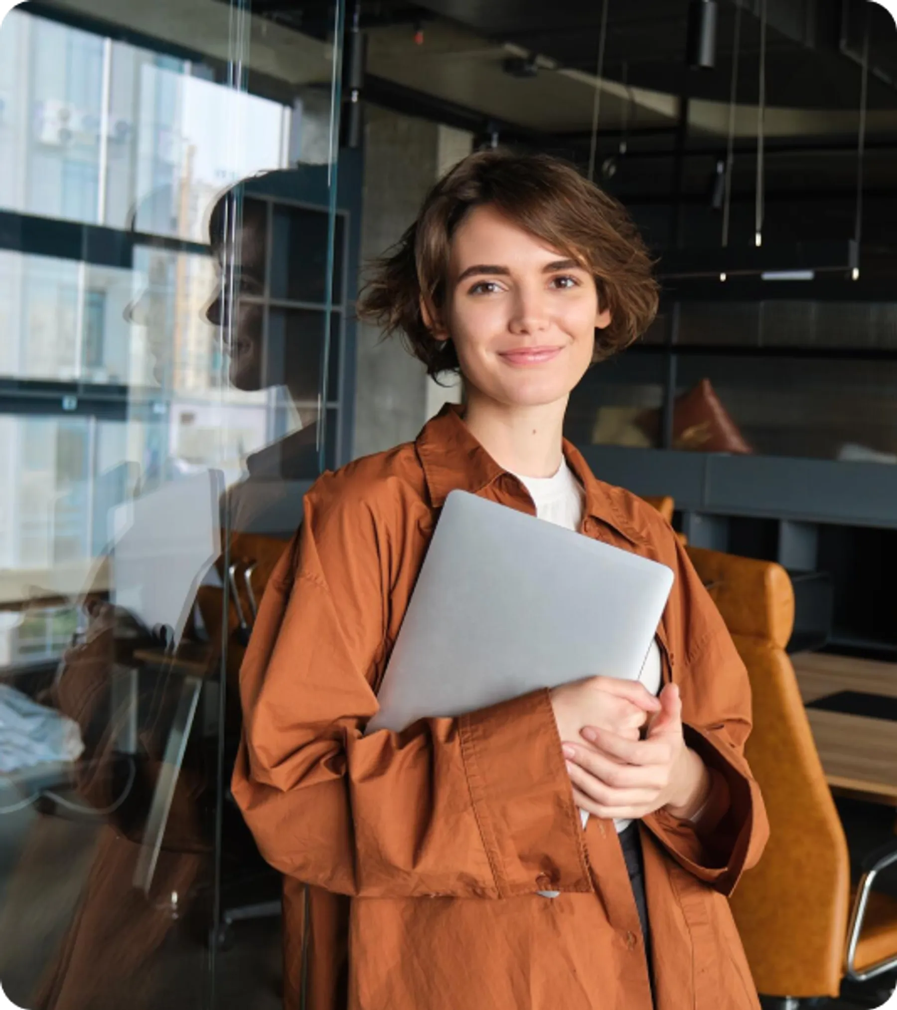 Young entrepreneur with short hair holding a laptop and smiling in a contemporary co-working space.