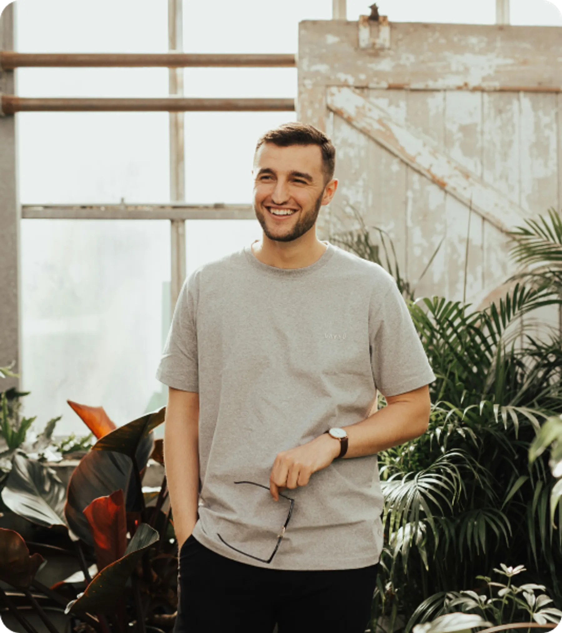 Smiling young man standing in a greenhouse setting, representing applicants for the UK Frontier Worker Permit visa